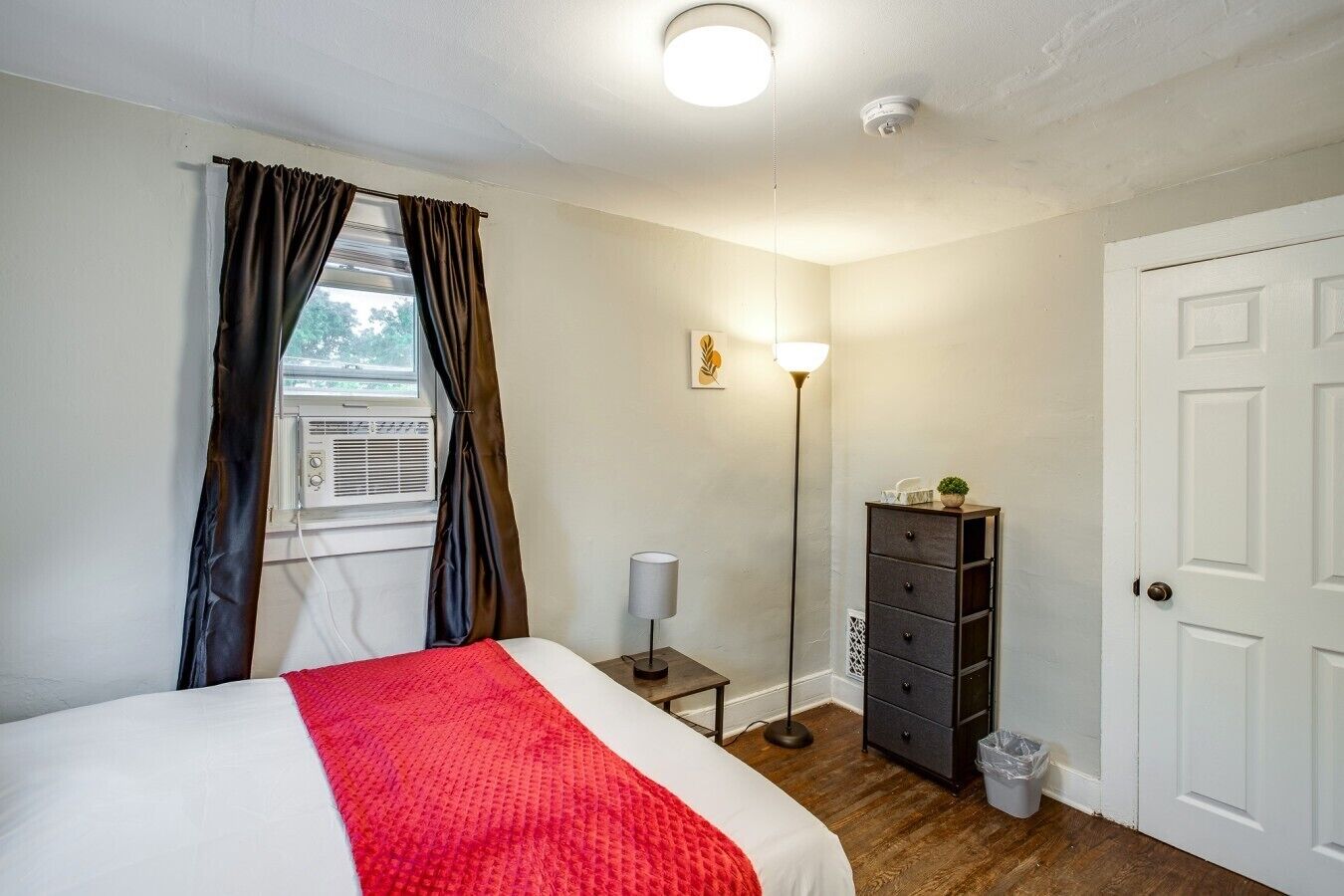 Una camera da letto con un letto, una lampada da comodino, un comò, una porta e una finestra con tende.