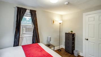 Una camera da letto con un letto, una lampada da comodino, un comò, una porta e una finestra con tende.