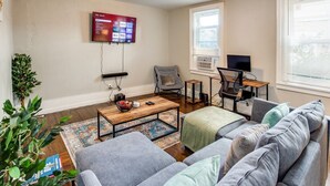 A living room with a TV, a desk with a computer, a couch, and a coffee table. - Downtown Rochester Home / 3 Bedrooms, Parking (Rochester)