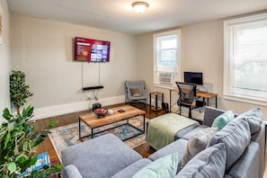 A living room with a TV, a desk with a computer, a couch, and a coffee table. - Downtown Rochester Home / 3 Bedrooms, Parking (Rochester)