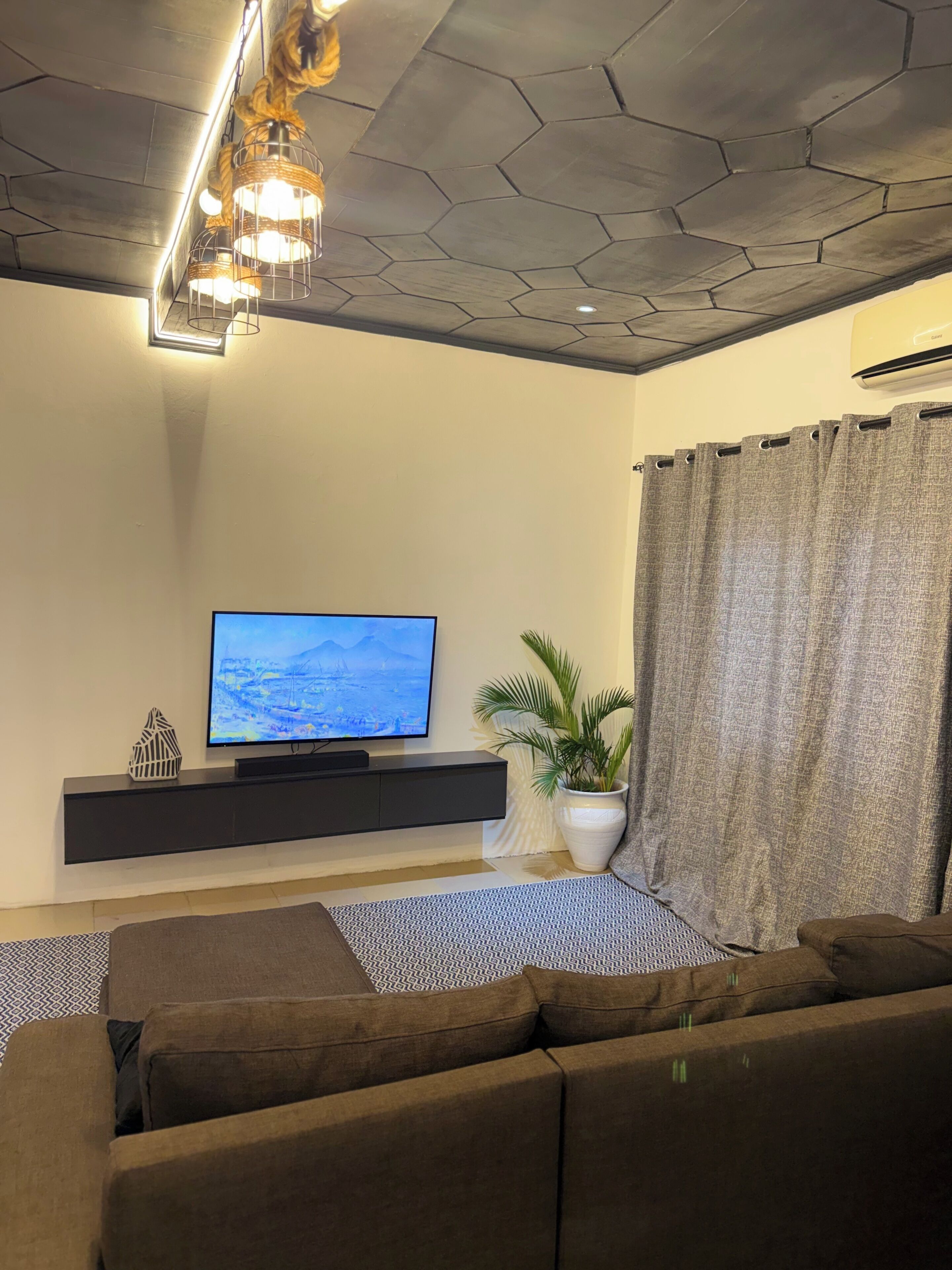 Ein modernes Wohnzimmer mit Flachbildfernseher, Sofa, Topfpflanze und einer dekorativen Leuchte.