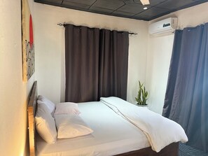 Un lit simple avec une literie blanche, une tête de lit et une plante en pot sur le côté.