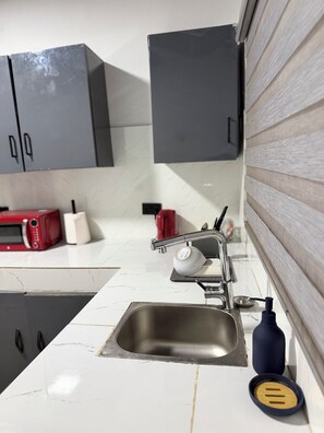 A kitchen with a stainless steel sink, a red microwave, and grey cabinets. - City Centre Oasis (Accra)