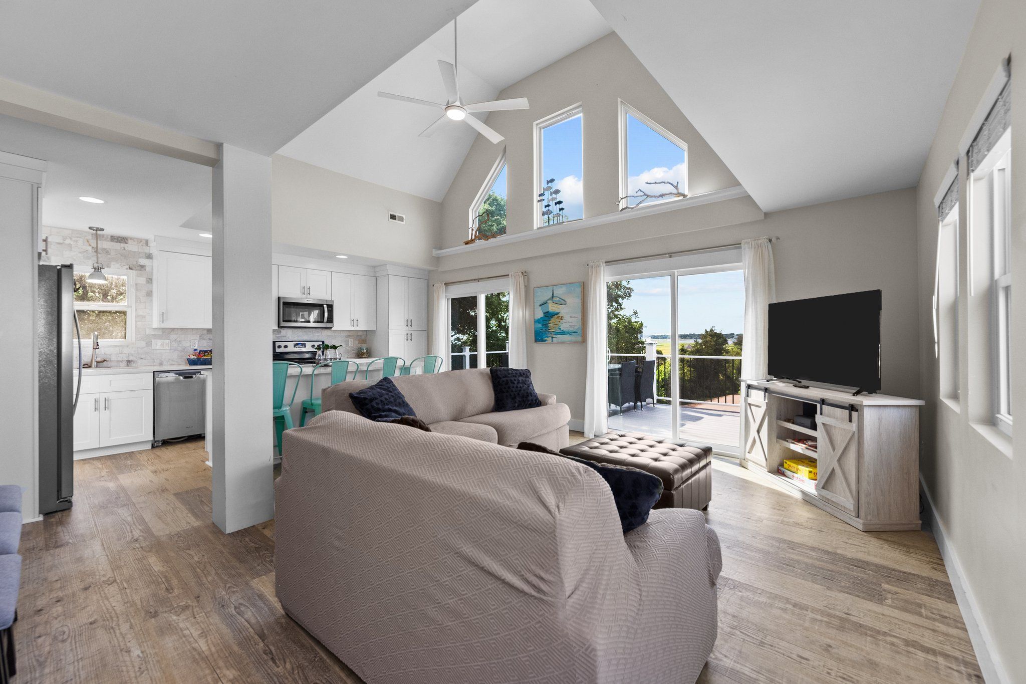 A spacious living area with a large sofa, a television, and a dining table. There is a kitchen in the background with white cabinets and a microwave.