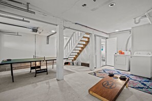 A room with a ping pong table, a wooden table with a logo, a washing machine, and a staircase. - Spacious 4-bedroom house in serene Surf City with AC (Surf City)