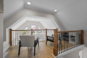 A spacious balcony with a wooden railing, a gray chair, and a black bench. - The Salted Rim | Sound Sunsets • 2-Min Walk to Beach • Bikes • Family Fun (Surf City)