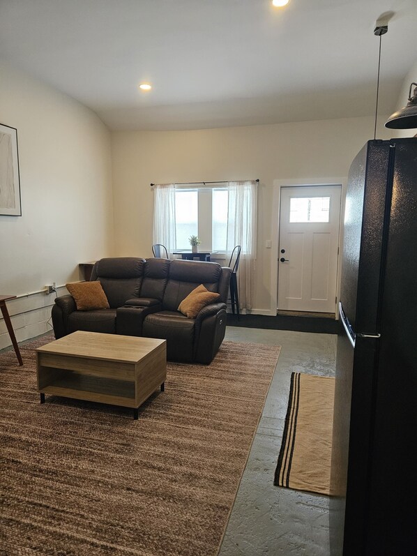 A living room with a sofa, a coffee table, and a black refrigerator.