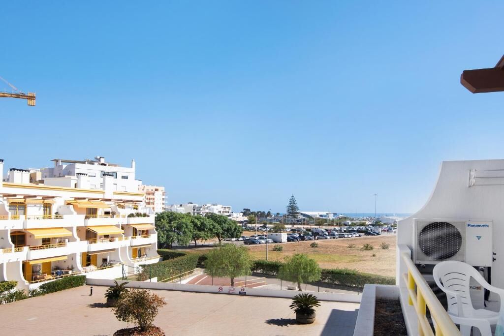 A residential building with multiple balconies, a parking lot, and a view of the sea.