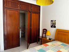 A bedroom with a bed, a nightstand, a chair, a lamp, and a wardrobe. - Apartment with Pool View and Private Balcony (Quarteira)