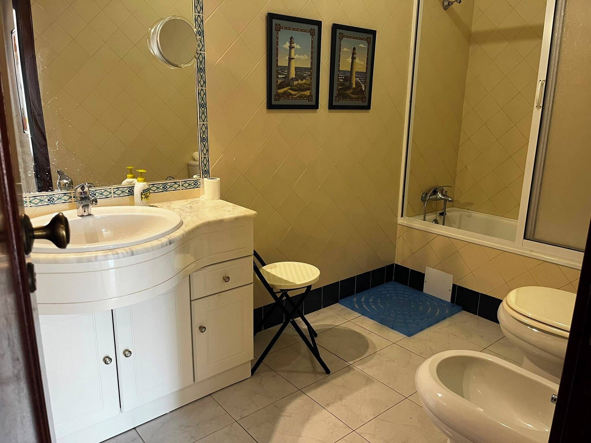 Baño con lavamanos, inodoro, bidé y un taburete pequeño.