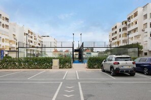 Un pàrquing amb dos cotxes, una entrada tancada i edificis residencials al fons.