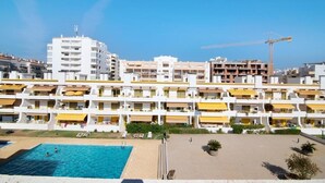 A multi-story hotel with balconies, a swimming pool, and a construction crane in the background. - Apartment with Pool View and Private Balcony (Quarteira)
