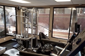 A gym with various exercise equipment, large windows, and a view of the outside.