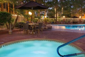A pool area with lounge chairs, umbrellas, and a table.
