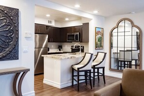 A modern kitchen with dark cabinetry, stainless steel appliances, a marble island, and two bar stools.