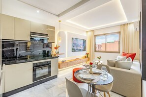 A modern kitchen with a dining area, a sofa, and a window with curtains. - Cosy 1BR Apartment in Guéliz, Free Parking, Near Carré Eden Mall (Marrakesh)