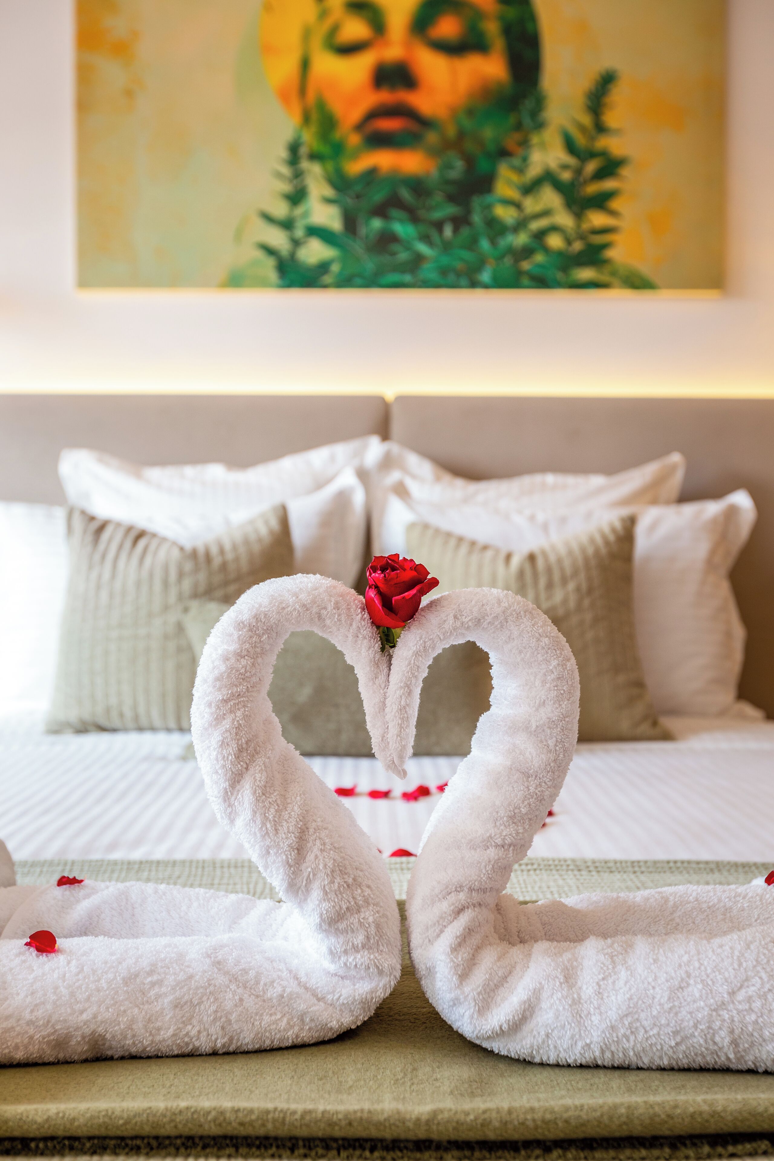 A hotel room with a bed, pillows, and a decorative towel arrangement in the shape of swans with a rose.