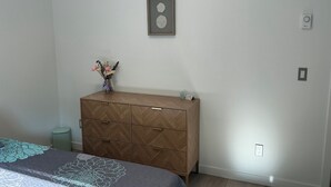 Een slaapkamer met een bed, een kaptafel, een vaas met bloemen en een wandklok.