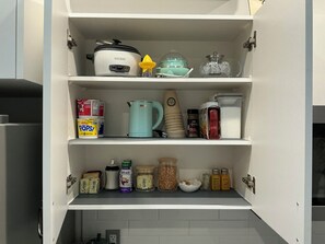 Un armario de cocina con una olla de cocción lenta, un hervidor y diversos alimentos.