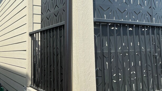 Een huis met een omheind portaal, een houten bankje en een metalen poort met geometrische patronen.