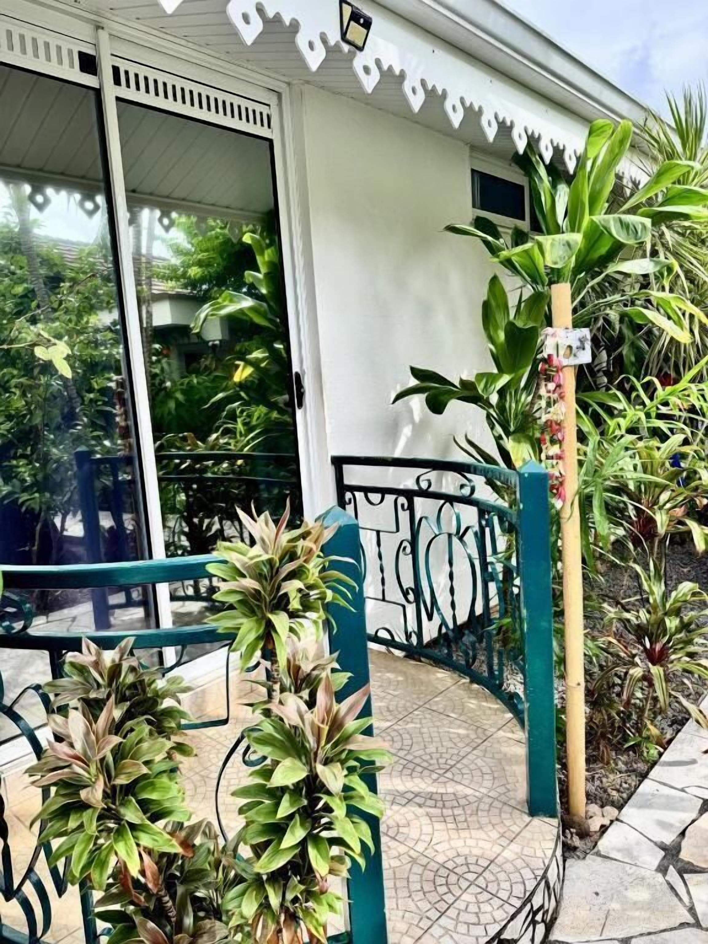 A building with a white exterior, a glass door, and a metal railing. There are potted plants and a small garden area with a variety of greenery.