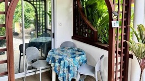 Un espacio al aire libre cubierto con mesas y sillas, un portón de madera y plantas en macetas.