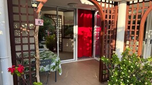 Una entrada con reja y puerta corredera de vidrio, una mesa con mantel estampado y plantas en macetas.