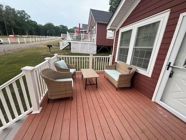 Una terraza de madera con muebles de mimbre y barandilla blanca.