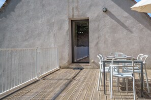 Eine Terrasse mit Tisch und Stühlen, ein weißer Zaun und ein Gebäude mit strukturierter Wand.