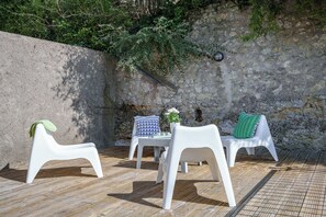 A patio area with white plastic chairs and a table, set against a stone wall with greenery. - Charming duplex with a pool near Amboise, sleeps 5 (including 1 baby) (Pocé-sur-Cisse)