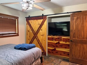 A bedroom with a bed, a TV, a ceiling fan, and a sliding barn-style door. - Cabin-Style Lake House (Eufaula)