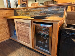 A wooden cabinet with a built-in mini-fridge containing beverages. - Cabin-Style Lake House (Eufaula)