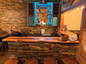 A bar area with a stone wall, a neon sign, a sink, and stools. - Cabin-Style Lake House (Eufaula)