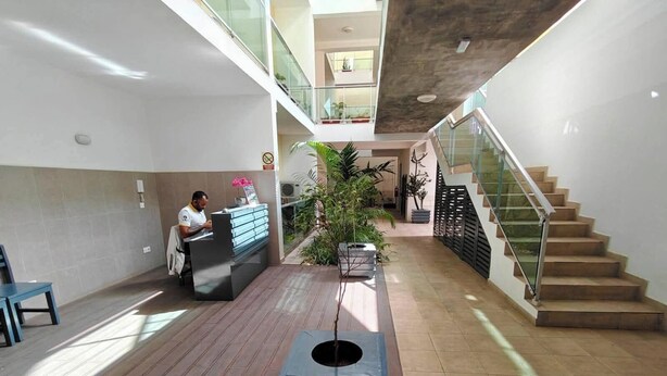 Una hall d'albergo con una reception, una scala e piante in vaso.