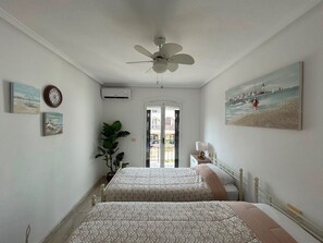 Ein Hotelzimmer mit zwei Betten, einem Deckenventilator, einer Uhr und einem Bild mit Strandmotiv.