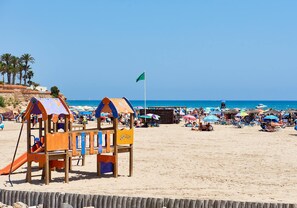 Ein Strand mit einer Holzspielanlage, Sonnenschirmen und blauem Himmel.
