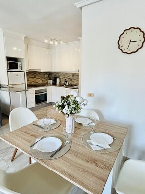 A dining area with a wooden table set for four, white chairs, and a vase of flowers.