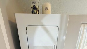 A compact laundry room with a front-loading washer and dryer, a small trash bin, and a door with a silver handle.