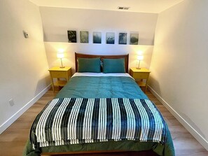 A bedroom with a bed, two bedside tables, a headboard, and wall-mounted artwork. - Modern and Bright Lynn Valley Retreat (North Vancouver)