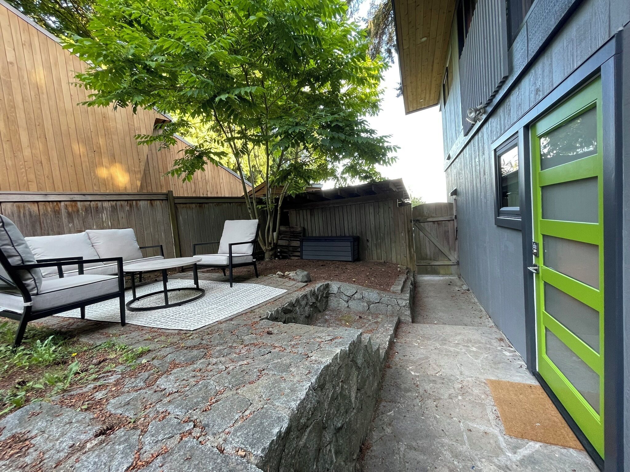 Un espace patio aménagé avec du mobilier d’extérieur, une clôture en bois et un bâtiment doté d’une porte verte.