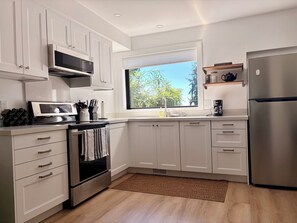 Eine moderne Küche mit weißen Schränken, einem Edelstahl-Kühlschrank und einem Fenster mit Blick auf Grünfläche.