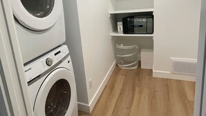 A laundry room with two stacked washing machines, a microwave, and a shelf with a trash bin. - Modern and Bright Lynn Valley Retreat (North Vancouver)