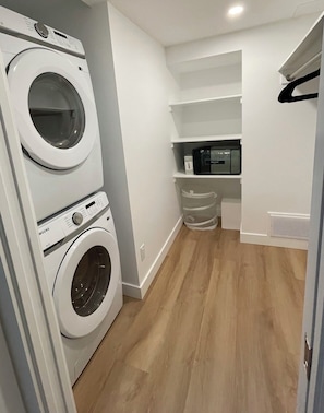 A laundry room with two stacked washing machines, a microwave, and a shelf with a trash bin. - Modern and Bright Lynn Valley Retreat (North Vancouver)