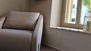 Un rincón de una habitación con una silla color beige, una ventana con persianas y una planta pequeña en el alféizar.