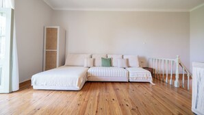 Un dormitorio con suelo de madera, una cama con ropa de cama blanca, un armario alto y una escalera.