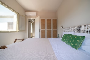 Ein Schlafzimmer mit Bett, Fenster, Tür und einer wandmontierten Klimaanlage.