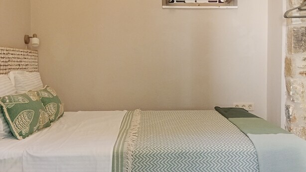 Una cama con un edredón estampado, almohadas y una lámpara fijada a la pared.