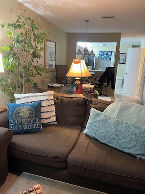 A living room with a brown sofa, a glass coffee table, a lamp, and a plant. - Few minutes walk  to beach and pool. Few-minutes drive to historic district. (St. Augustine)