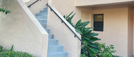 Un immeuble résidentiel doté d’un escalier en béton, de nombreuses fenêtres et entouré de verdure.