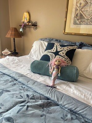 A bed with a mermaid doll, a lamp, a clock, and a framed picture on the wall. - Few minutes walk  to beach and pool. Few-minutes drive to historic district. (St. Augustine)
